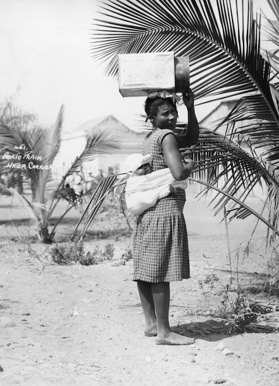 Circa 1950 - A water carrier, with a baby on her back, at Praia, in the Cape Verde Islands [Keystone/Getty Images]